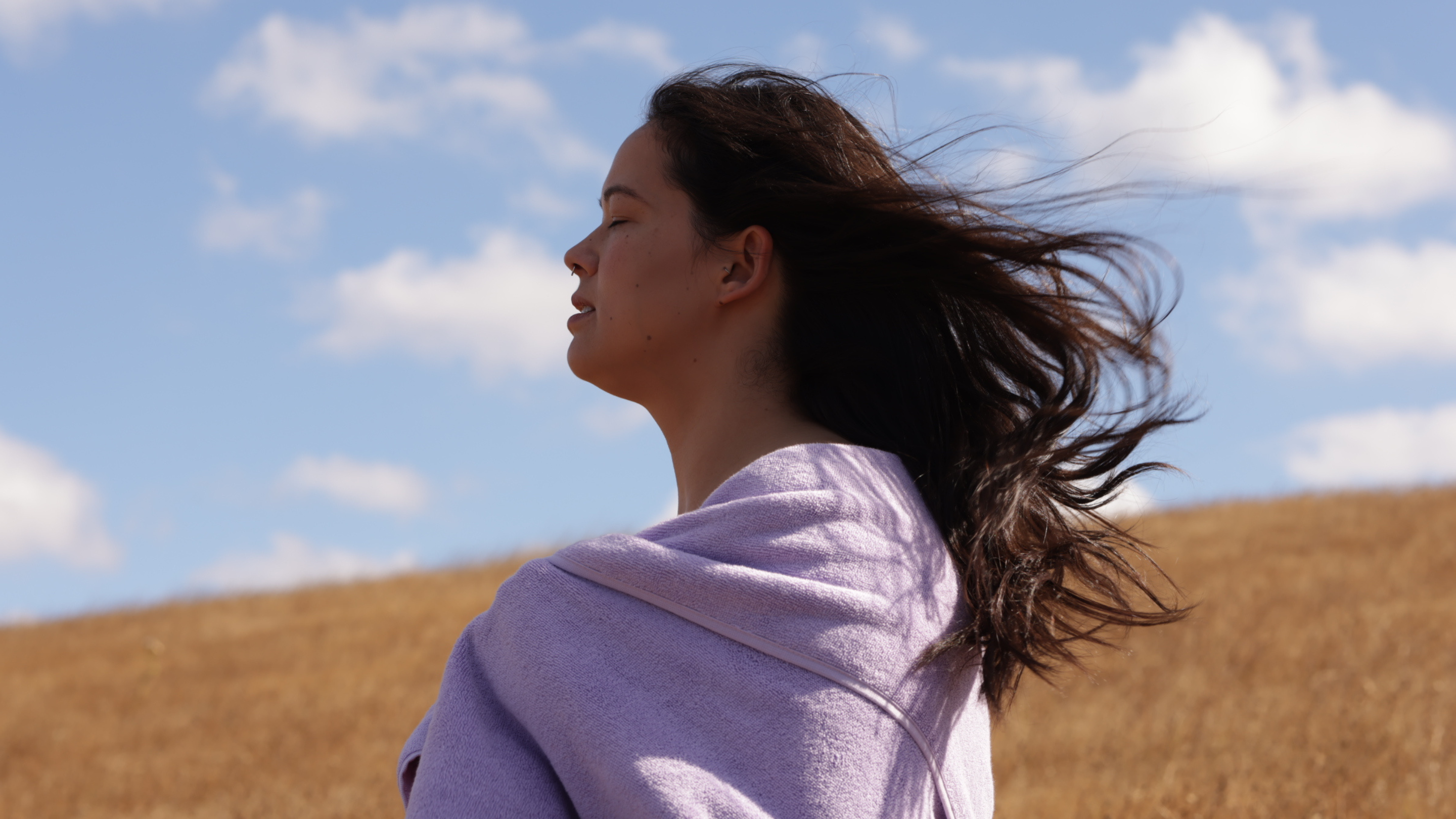woman with dark brown hair wrapped in a lilac bath towel in a field