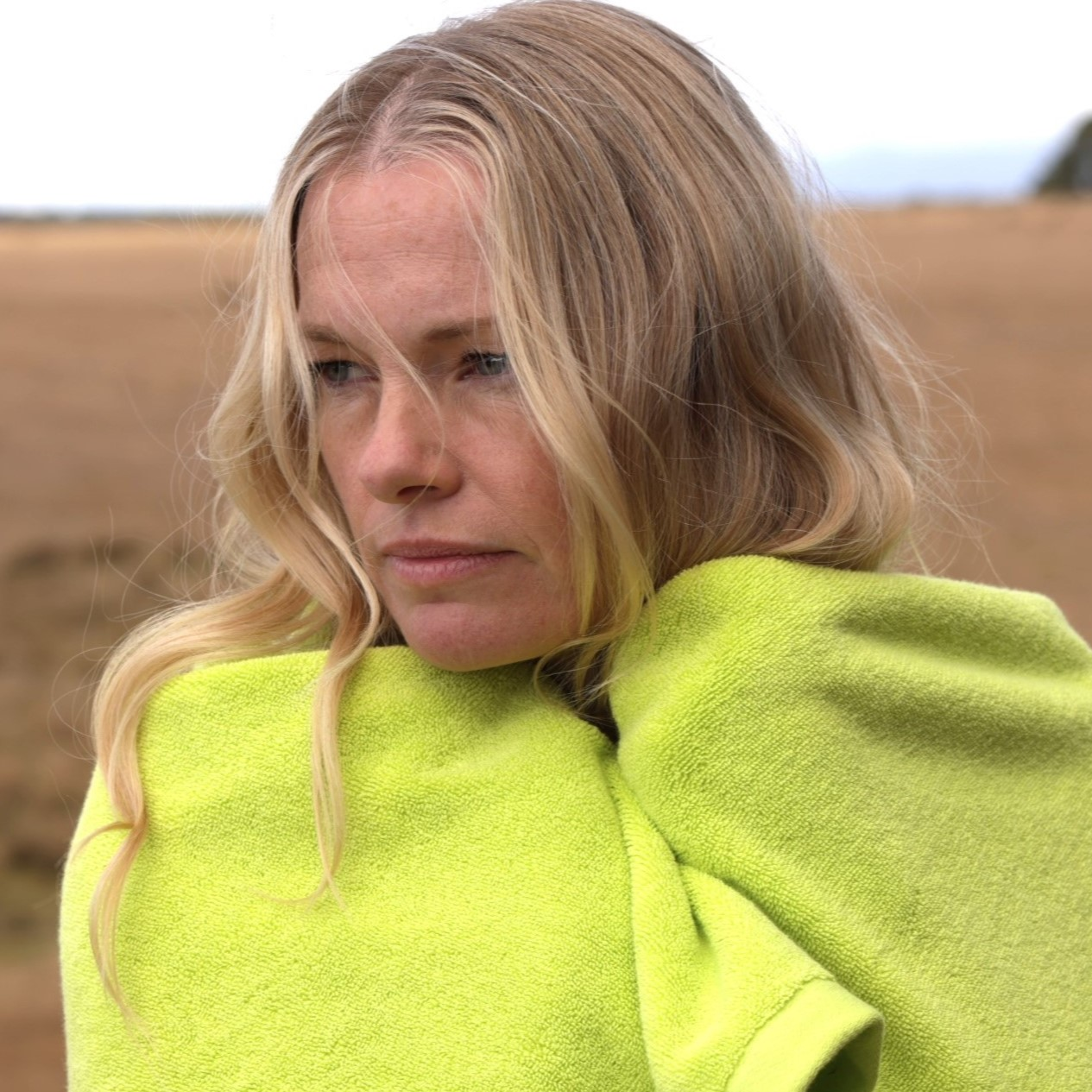 blonde woman wrapped in a chartreuse towel in a field