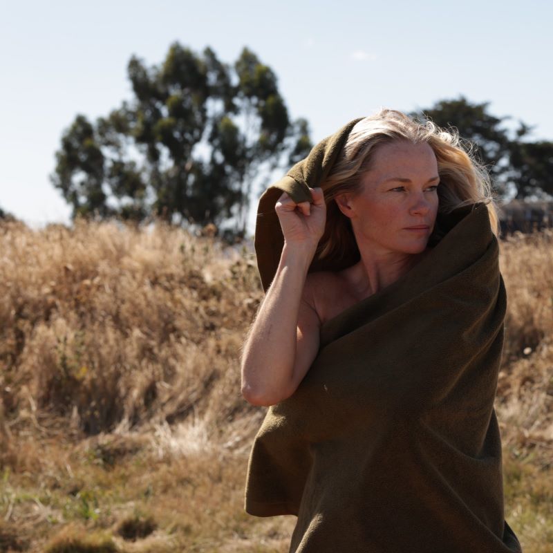 blonde woman holding a khaki towel around her in a field