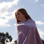 girl with blonde hair wrapped in a lilac bath towel  with blue sky behind her