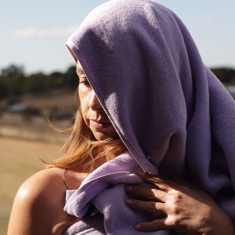 woman with bare shoulder draped in a lilac bath towel in a ray of sunlight