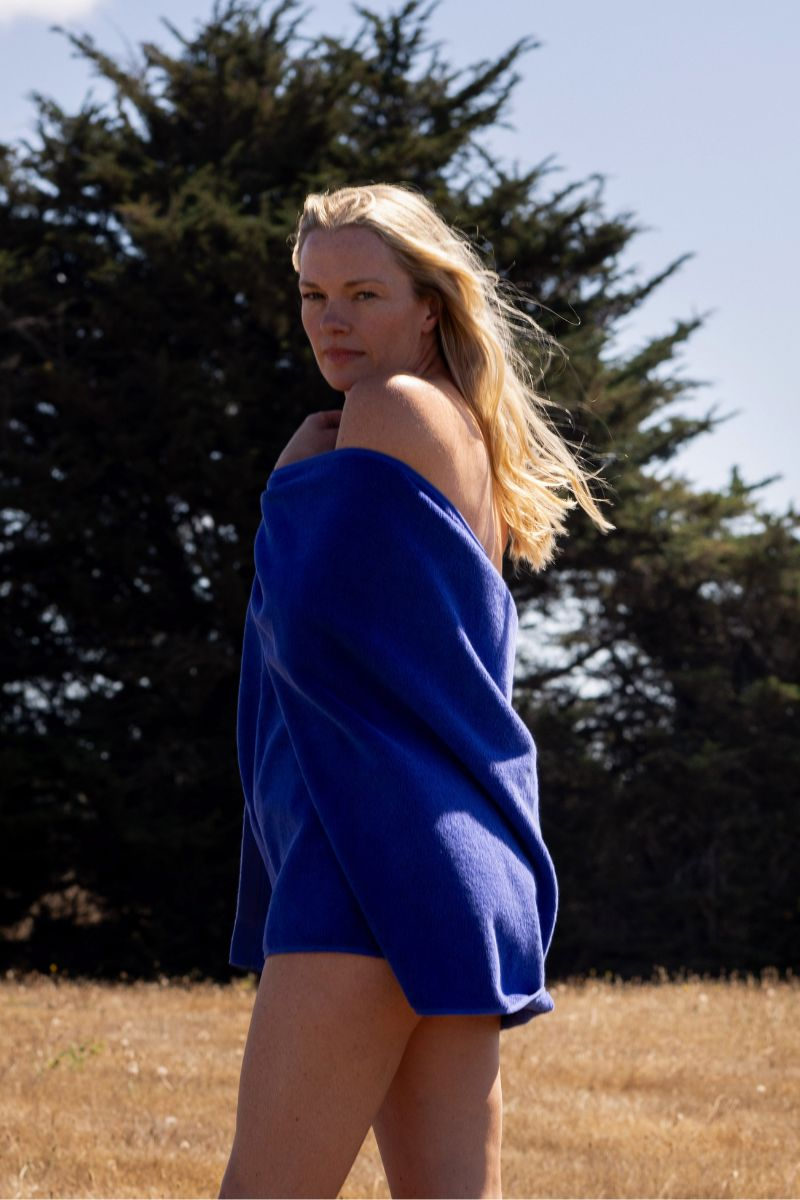 Blonde woman wrapped in electric blue bath towel against trees