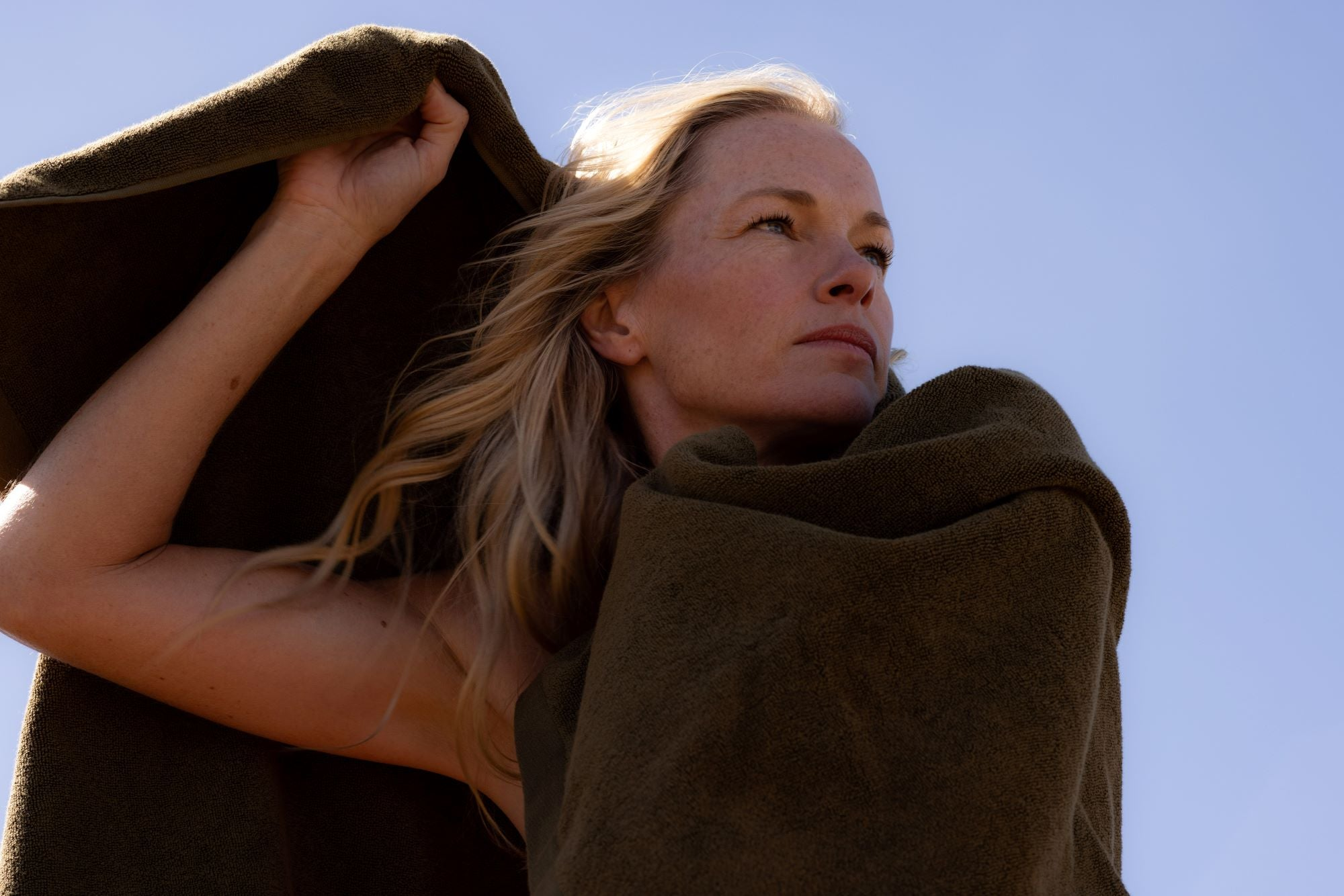 woman with blonde hair wrapped in a khaki towel with one arm above her head