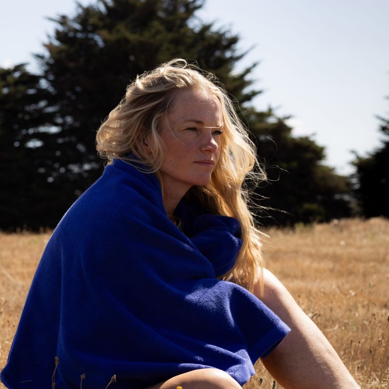 woman with blonde hair sitting in a field wrapped in an electric blue towel