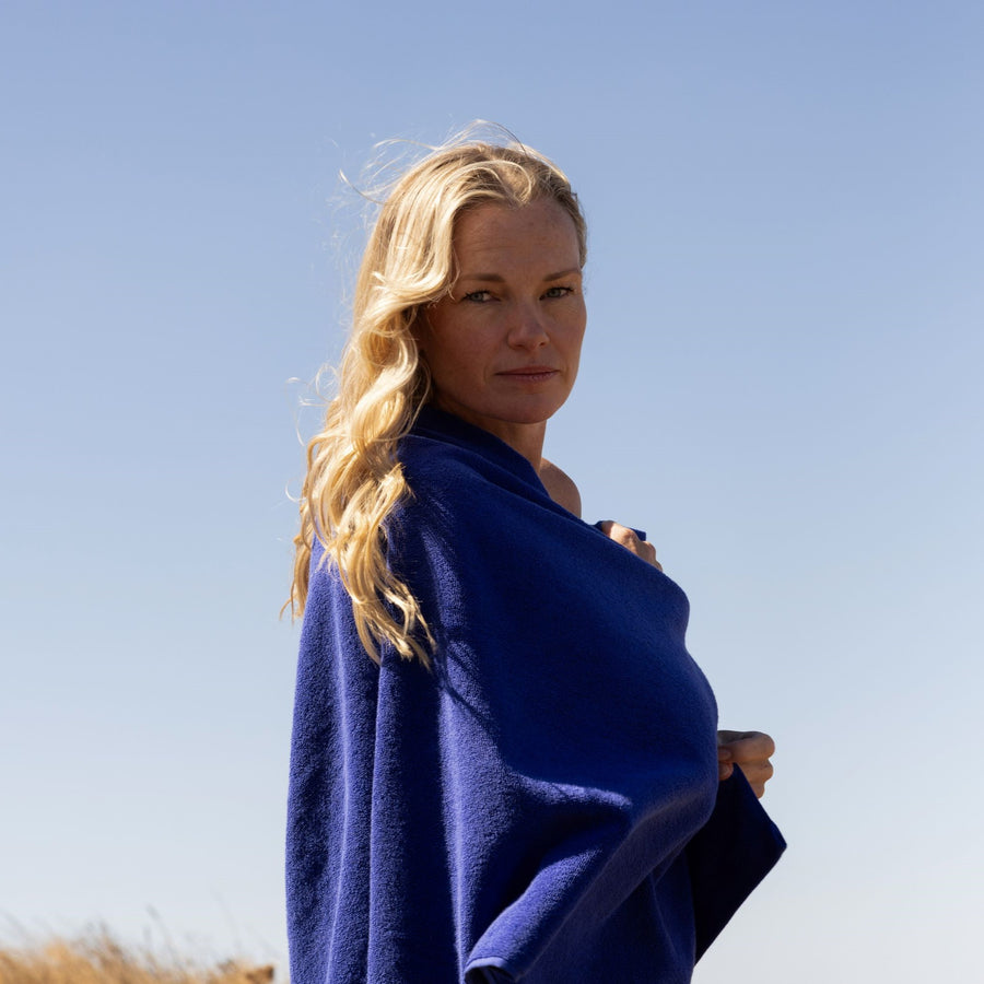 blonde woman wrapped in an electric blue towel with blue sky behind her