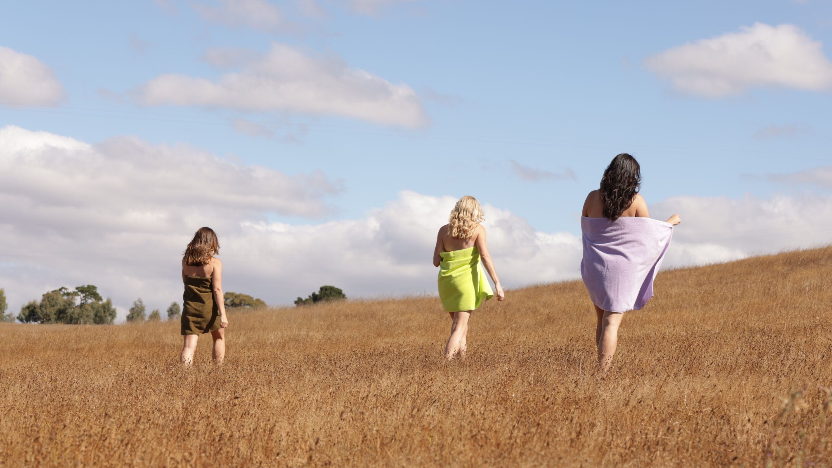 three women wrapped in bath towels in a field