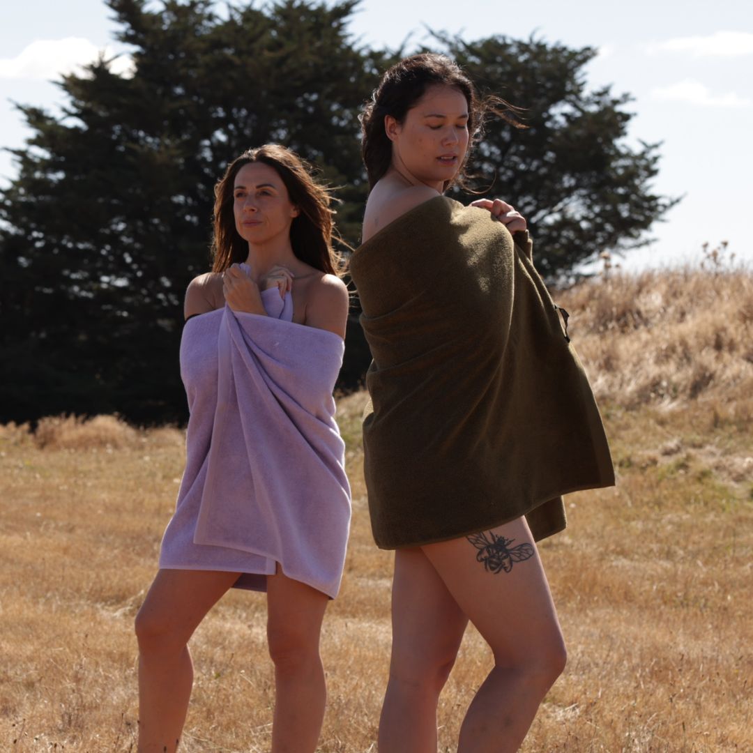 Two women wrapped in bath towels stand in a field