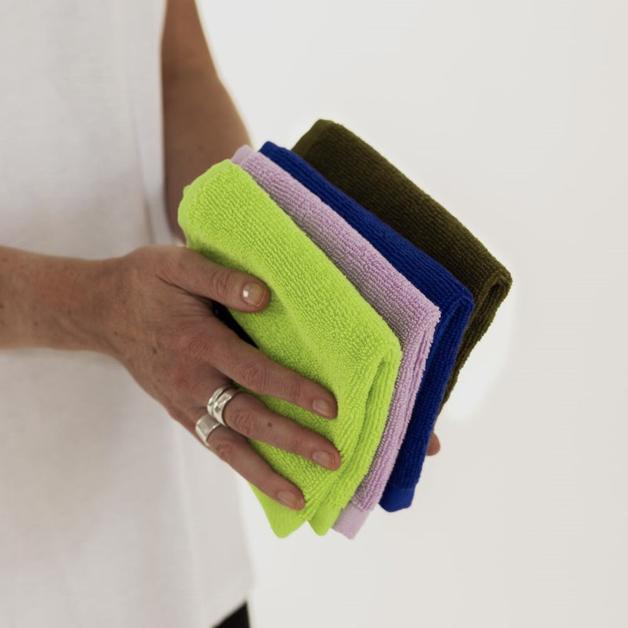 hands with silver rings holding folded chartreuse, lilac, electric blue and khaki face washers