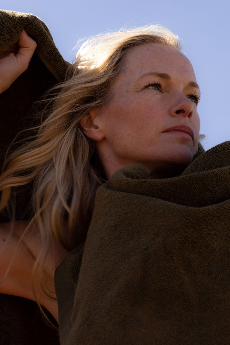 woman with blonde hair wrapped in a khaki bath towel with one arm above her head