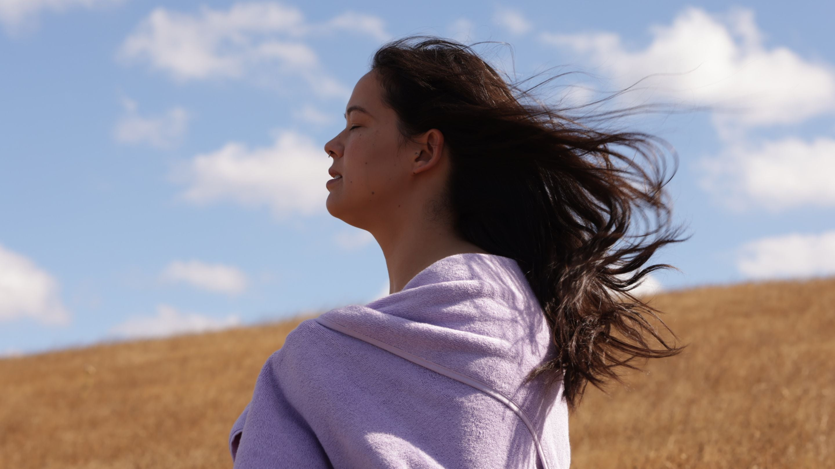 Woman with long dark brown hair hair wrapped in a lilac towel against a blue sky