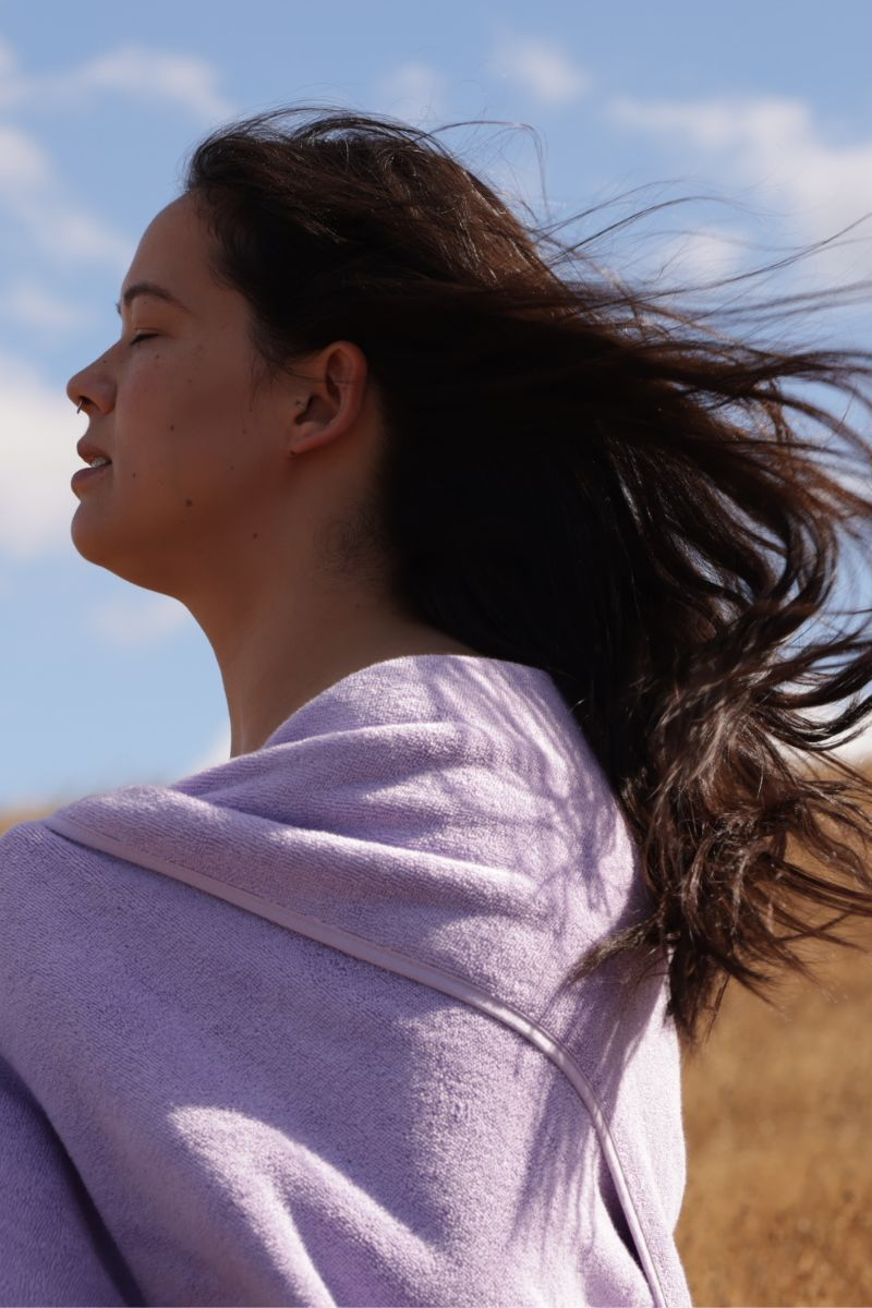 Woman with long dark brown hair hair wrapped in a lilac towel against a blue sky