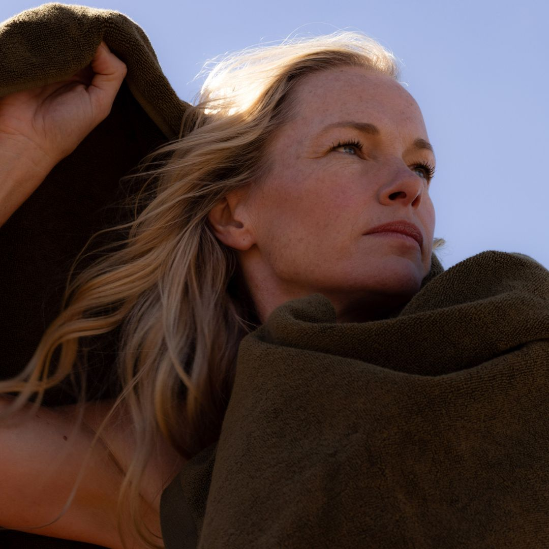 blonde woman wrapped in khaki  bath towel against blue sky